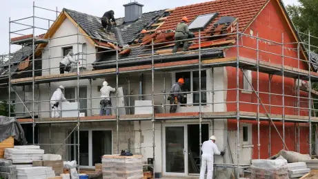 dach-fassade-gebaeudehuelle Wohnhaus mit Gerüst während Dach- und Fassadenarbeiten mit mehreren Handwerkern auf Dach und Fassade